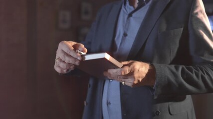 Mature businessman takes notebook and pen out of inner pocket at backlit closeup. Manager in formal jacket writes in notepad in office - Powered by Adobe