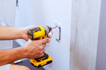 Electrician installs an outlet at wall using screwdriver during construction of house
