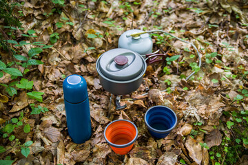 Fototapeta premium Coffee pot and metal cup on big stone against backdrop of mountain river. Coffee pot on stone plate over blurred nature background.