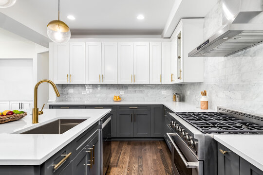 A luxurious white and grey kitchen with gold hardware, stainless steel appliances, and white marbled granite countertops. No brands or labels.