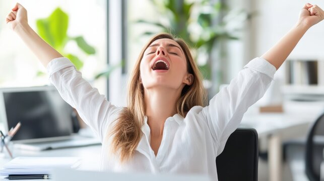 Young woman in office stretch with arms raised in joy, celebrating success or achievement, feeling happy and accomplished.