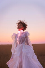Fototapeta premium A woman in a white dress stands in a field with a pink