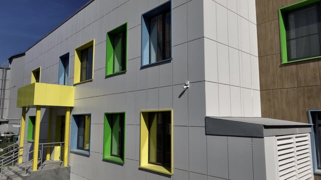 Windows in colored jambs line facade of preschool building. Practical grey tiles help conceal stains keeping building looking clean