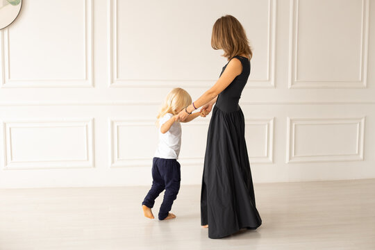 Mother and her little son dancing at home near white wall. Motherhood, affection