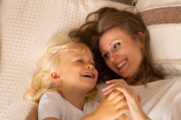 Portrait of happy laughing mother and her little child son baby boy hugging lying on bed at home. Motherhood, affection