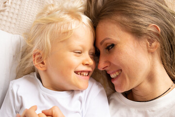 Portrait of happy mother and her little child boy hugging on bed at home. Motherhood, affection