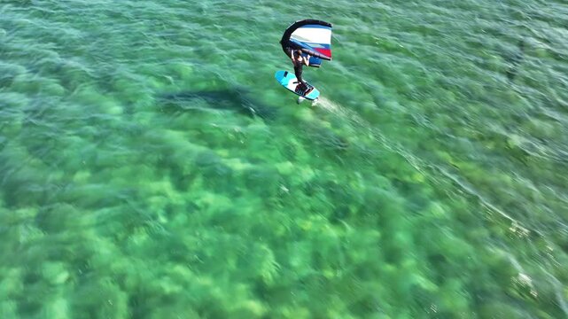 Aerial drone tracking video of fit athlete practise hydro foil wing surfing in tropical exotic island bay with crystal clear emerald sea