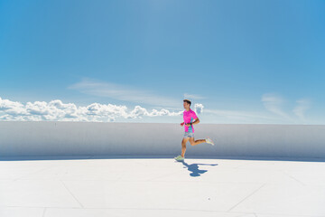 A man in a bright pink shirt and shorts runs energetically under a clear blue sky.