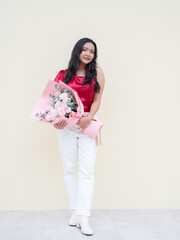 Beautiful smiling asian woman wearing a red dress is holding a bouquet of pink rose isolated on Cream color background.