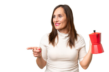 Middle-aged caucasian woman holding coffee pot over isolated background pointing to the side to present a product