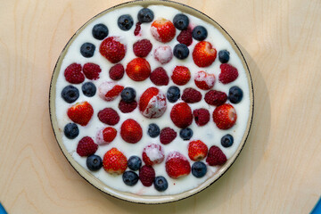 In a plate with whipped cream, strawberries, raspberries and blueberries on a gray table