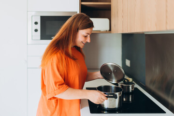 Young happy woman cooking at the kitchen, girl standing near stove at home. Domestic life and leisure moments. High quality photo. Beautiful female preparing tasty meal.