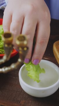 A Jewish woman in blue at the Pesach Seder table dips karpas in salt water. Vertical video