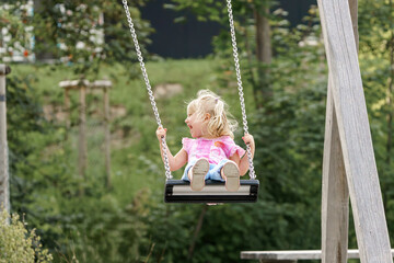 A little girl is riding on a chain swing in a park.