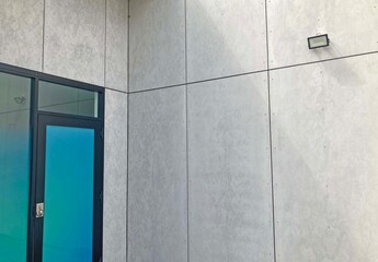 Abstract image of new grey fibre cement clad wall with a glass doorway and a light fitting