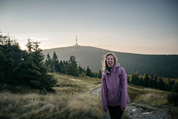 Young woman wearing a purple windproof jacket is having fun during a hike in mountains of central Europe