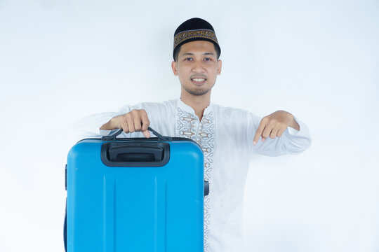 Moslem Asian man carrying suitcase with happy expression pointing below
