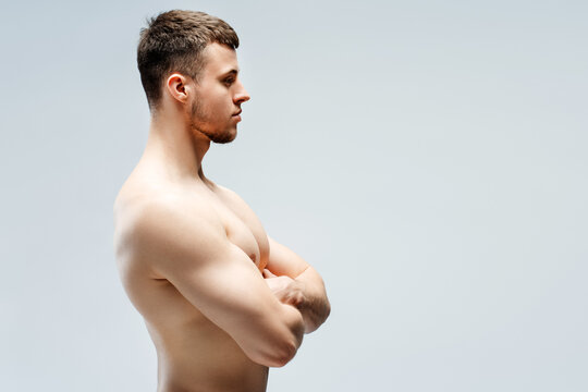 Fit man standing sideways crossing arms showing muscles, looking away isolated on gray background