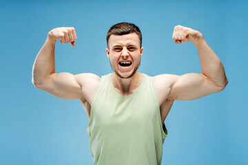 Fototapeta premium Young athletic man showing muscles and screaming standing isolated on blue background