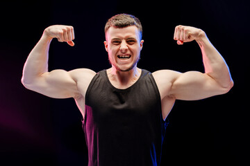 Bodybuilder man flexing muscles showing his strength, looking at camera isolated on black background