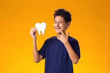 Child boy holding papercraft tooth and pointing finger at mouth. Dental health concept