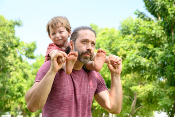 Obraz premium little boy play with dad on summer day. father carries his son on his shoulders in park. father day happy family child dream concept.