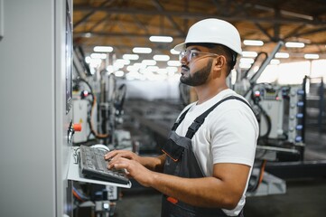 Operator of machine. Industrial worker indoors in factory. Young technician in white hard hat