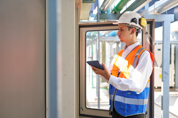 Engineer or worker working at machine control panel and checking pipeline valves or water tank area at urban industrial site