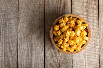 Sweet caramel popcorn in a bowl on a wooden background. Salted caramel popcorn. Caramel sauce. Close up. Topping. Place for text. Copy space