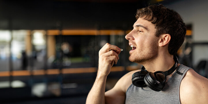Sportive man taking supplement capsule, eating omega 3 or amino acid multivitamin pill, gym interior