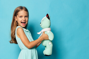 Little girl in a white dress hugging a teddy bear on a vibrant blue background, radiating innocence and joy