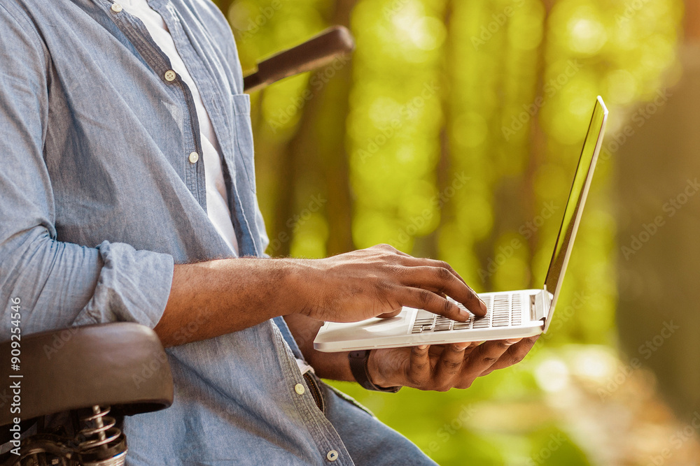 Poster always in touch. unrecognizable african american man using laptop while riding bicycle in forest