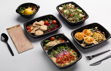 Healthy lunch at workplace. Take away meals in black containers with cutlery on gray table