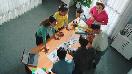 Top down aerial view of skilled designer hold logo while discuss with team. Aerial business group working together sharing idea about logo graphoic design by using sticky notes and tablet. Symposium.