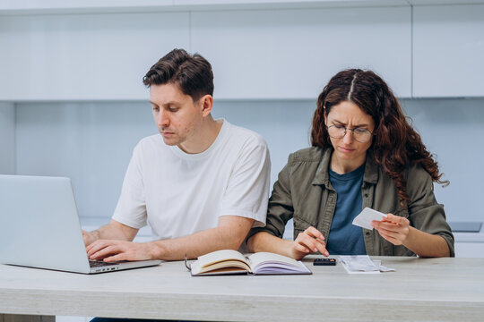 Couple working together on finances at home, with a laptop, notebook, and calculator, focused on budgeting and expenses. Woman counts and writes down expenses in a notebook.