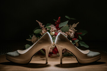 Obraz premium Cesis, Latvia - July 12, 2024 - Two high-heeled shoes positioned back to back with a wedding ring balanced between them, set against a vibrant floral bouquet in low light.