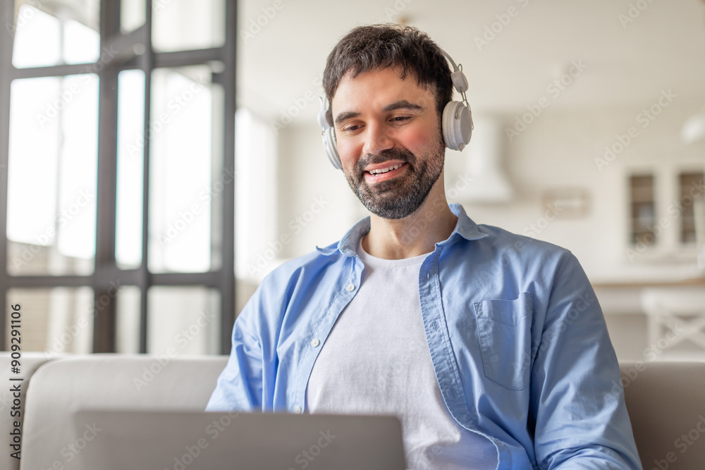 Aufkleber a man sits on a white couch in a living room with a window behind him. he is wearing headphones and 