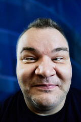 Fototapeta premium Close-up portrait of fat man crossed his eyes to bridge of his nose, face of white man 47 years old on blue background.