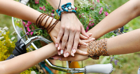 Girl Friendship. United hands of young females. Stylish girlfriends in boho hippie bracelets near bicycle handlebar, top view. Togetherness and support, youth fashion and active lesiure. © Prostock-studio