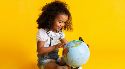 Cute little girl looking at earth globe over yellow studio background