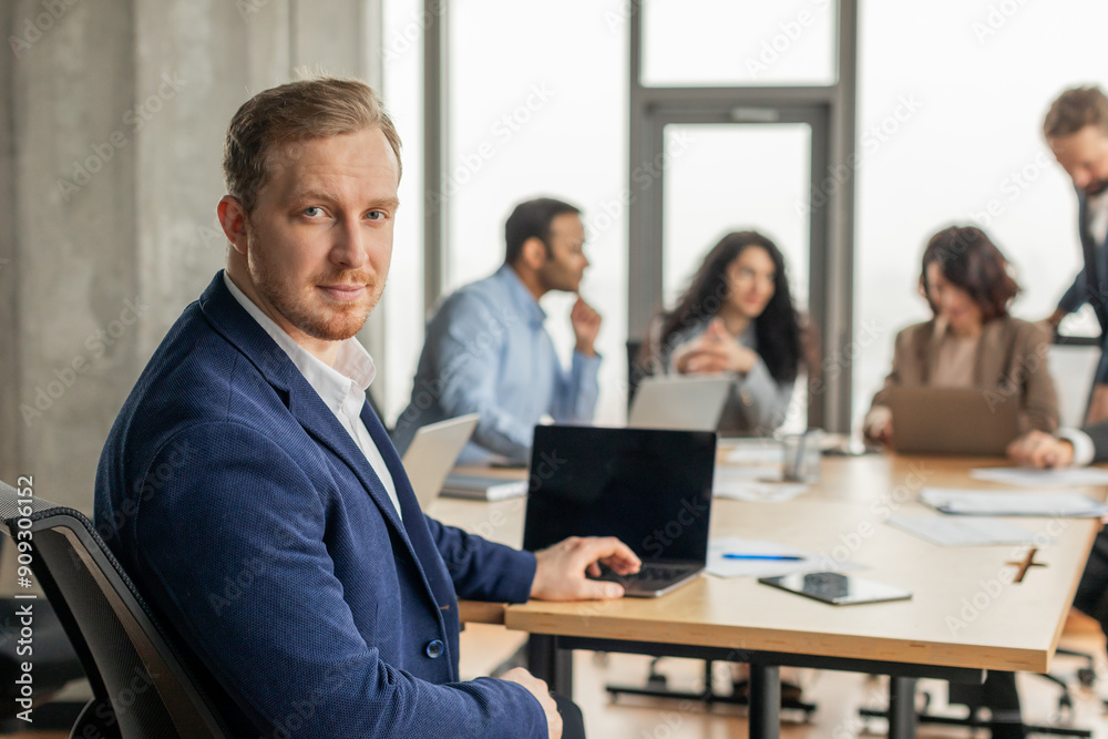 Fototapete a young businessman in a blue suit is working at a desk in a modern office. he is looking directly a