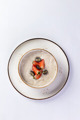 Porridge with milk with berries in a plate on a white background.