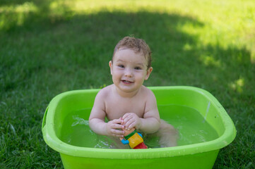 Cute baby boy bathes in a basin outdoors in summer.