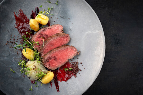Traditional fried venison back filet with sliced pear, gnocchi and plum jam served as close-up on Nordic design plate with copy space right
