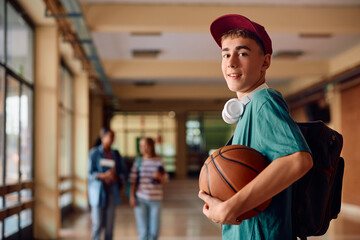 Happy teenage boy with basketball at high school looking at camera.