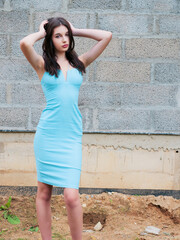 A woman in a blue dress is standing in front of a brick wall. Concept of elegance and sophistication, as the woman is dressed in a beautiful blue dress and poses confidently.