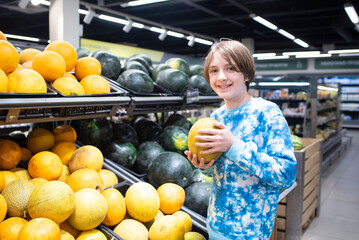 Obraz premium Portrait of a smiling boy choosing melons in the supermarket