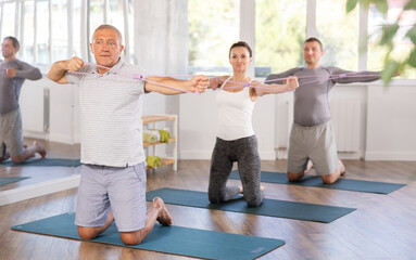 Fototapeta premium Elderly man doing pilates exercises with elastic loop in group in fitness studio