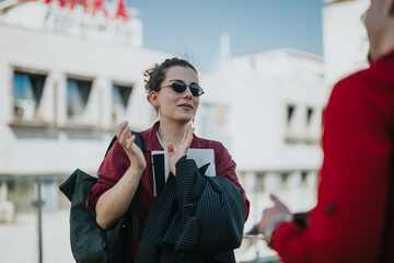 A businesswoman chatting outdoors in the city, holding documents and wearing sunglasses. Casual, relaxed atmosphere on a sunny day.