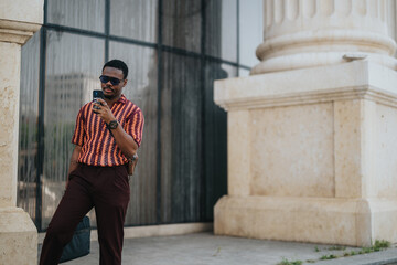 Confident man in stylish outfit using smart phone outdoors near modern architecture building. Checking messages or working on the go.